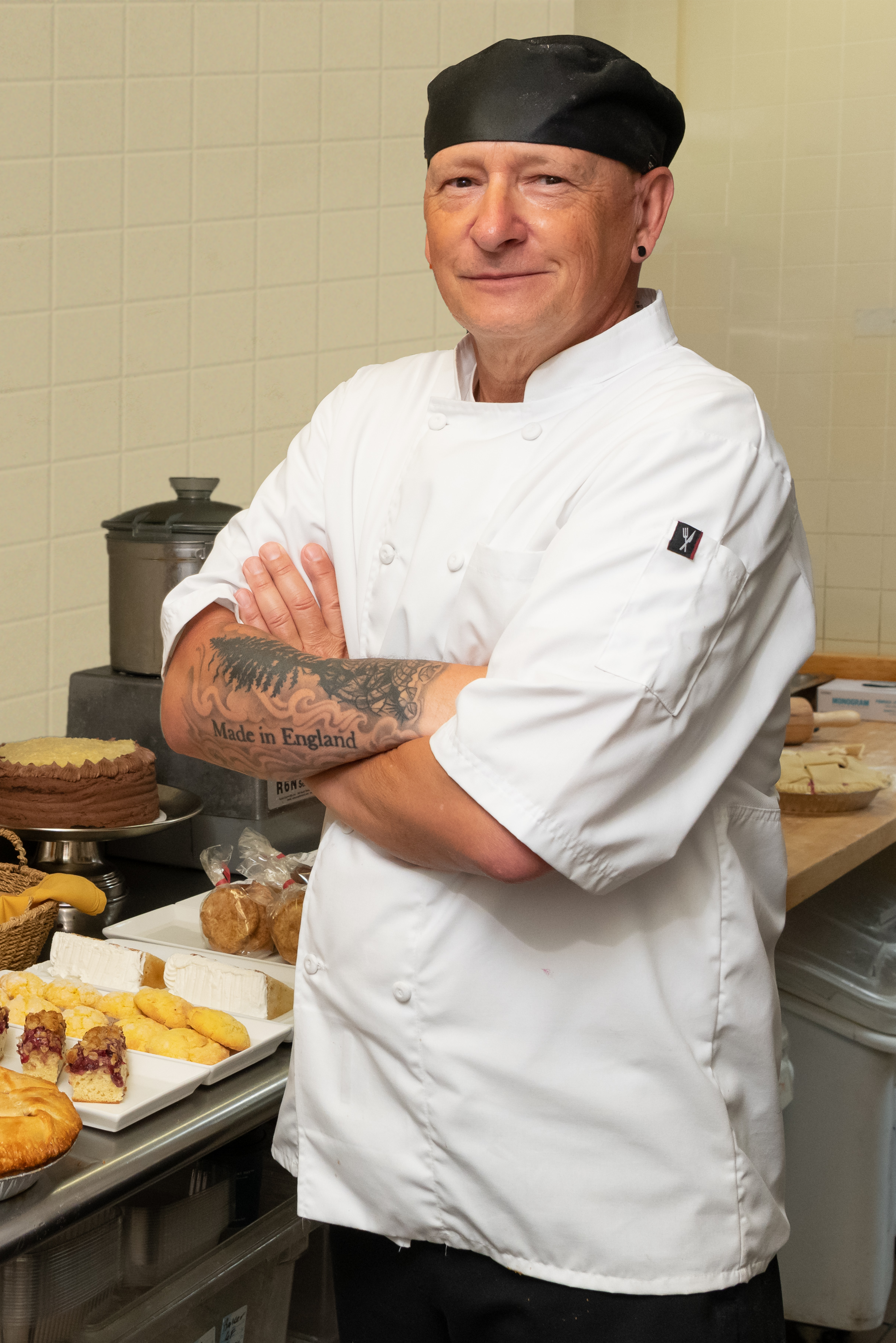 Robin Flower, Laurel Parc's Executive Chef, posing and smiling for a photo in front of a kitchen counter full of pastries.